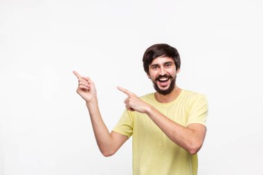 Sakallı sarı gömlekli yakışıklı brunet adam ve bıyıkları parmaklarıyla işaret sol tarafında beyaz arka plan üzerinde izole ayakta. Ürün ve reklam yeri.