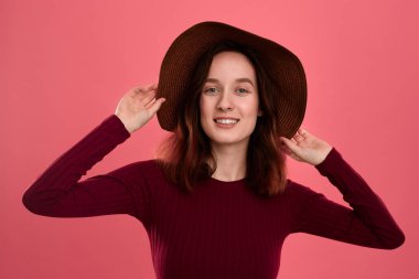 Koyu pembe arka plan üzerinde poz geniş kenarlı şapka mutlu bir güzel esmer kız Portresi.