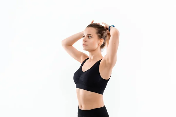 Mujer rubia deportiva bastante joven en una ropa deportiva negra fija el cabello antes de hacer ejercicio aislado sobre fondo blanco . — Foto de Stock