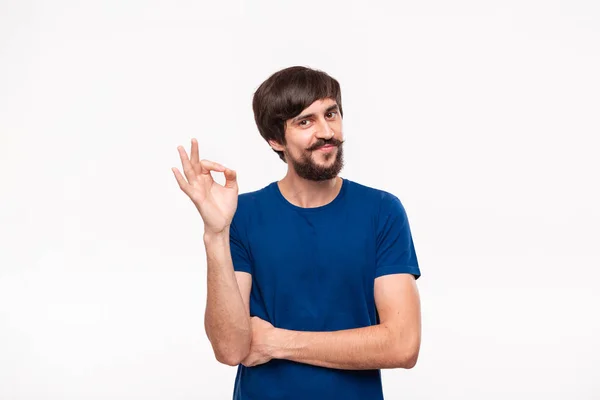 Handsome brunet bearded man with mustaches in a blue shirt showing gesture of OK sign standing isolated over white background. OK gesture. — Stock Photo, Image