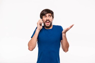 Sakallı mavi gömlekli pretty brunet adam ve çoğu ağrıları beyaz arka plan üzerinde izole duran kamera bakarak akıllı telefon tutarak şok. Sürpriz duygusu. Telefondan beklenmeyen haberler.