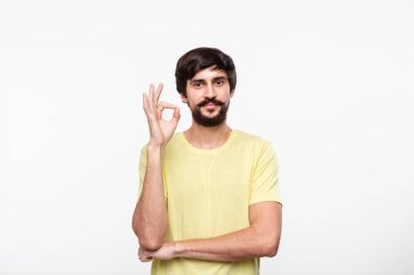 Yakışıklı brunet sakallı adam sarı gömlek bıyıklı ok işareti gösteren beyaz arka plan üzerinde izole ayakta. Tamam hareketi.