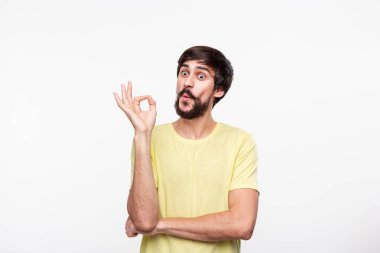 Yakışıklı brunet sakallı adam sarı gömlek bıyıklı ok işareti gösteren beyaz arka plan üzerinde izole ayakta. Tamam hareketi.