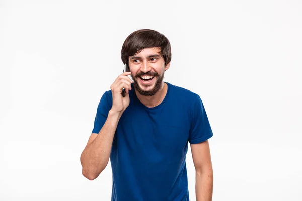 青いシャツにあごひげを生やしたハンサムなブルネットの男は、白い背景の上に孤立したスマートフォンで話す笑顔を見せた。コミュニケーションの概念。電話で良い知らせ. — ストック写真