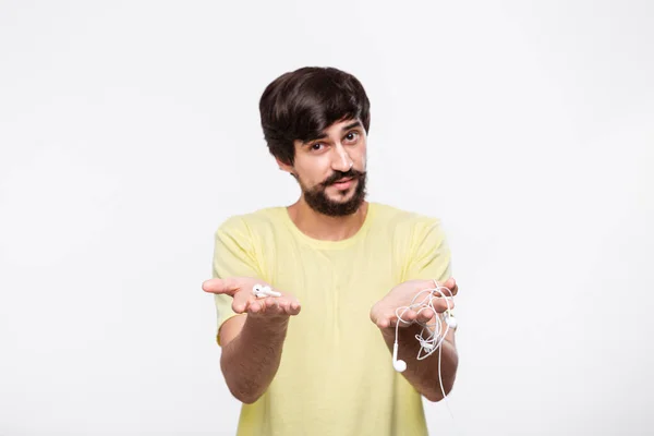 Bıyıklı pretty brunet sakallı adam bir elinde kablolu kulaklık tutar ve diğer kablosuz kulaklıklar. İstediğini seç. Kablosuz kulaklıklara yükseltme zamanı.