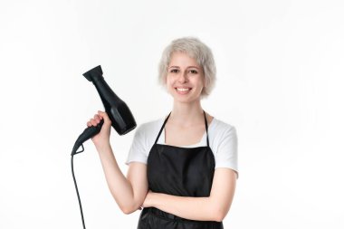 Beyaz tee ve siyah önlük profesyonel siyah saç kurutma makinesi beyaz arka plan izole iş için hazır tutan genç güzel kuaför. Sağlıklı yaşam endüstrisi ve profesyonel kariyeri.