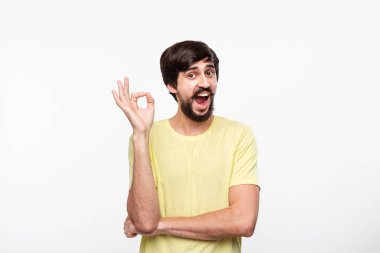 Beyaz arka plan üzerinde izole duran Ok işareti jest gösteren sarı gömlek bıyıklı yakışıklı brunet sakallı adam.