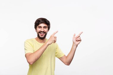 Sakallı sarı gömlekli yakışıklı brunet adam ve bıyıkları sağ tarafına parmaklarıyla beyaz arka plan üzerinde izole ayakta işaret. Ürün ve reklam Yeri.