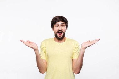 Sakallı sarı gömlekli heyecanlı brunet adam ve çoğu omuzlarını silkerek beyaz arka plan üzerinde izole ayakta şaşırıyor.