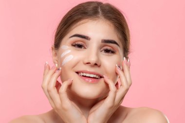 Güzel model pembe arka plan üzerinde izole bir hyaluronik krem beyaz tüp tutan cilde nemlendirici kozmetik ürün uygular. Güzellik ve sağlık tedavisi kavramı.