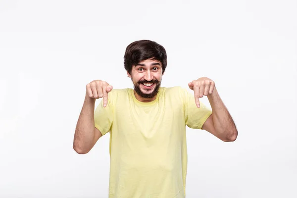 Stilig Brunet man i en gul skjorta med skägg och mustascher pekar med fingrarna ner stående isolerad över vit bakgrund. Plats för produkt och annons. — Stockfoto