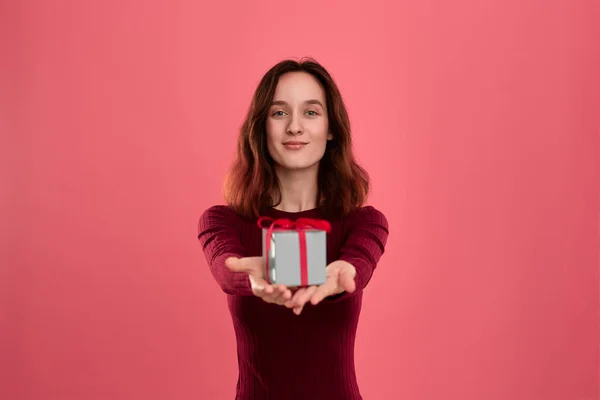 Podekscytowany Ładna Brunetka trzyma obecne pudełko z wstążką z dwoma rękami stojący odizolowany na ciemnym różowym tle i uśmiechnięty do aparatu. Uroczysta impreza specjalna. — Zdjęcie stockowe