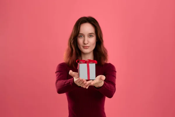 Podekscytowany Ładna Brunetka trzyma obecne pudełko z wstążką z dwoma rękami stojący odizolowany na ciemnym różowym tle i uśmiechnięty do aparatu. Skoncentruj się na pudełku. Uroczysta impreza specjalna. — Zdjęcie stockowe