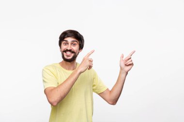 Sakallı sarı gömlekli yakışıklı brunet adam ve bıyıkları sağ tarafına parmaklarıyla beyaz arka plan üzerinde izole ayakta işaret. Ürün ve reklam yeri.