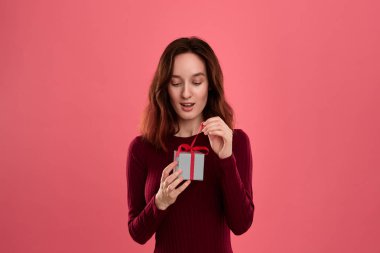 Heyecanlı güzel esmer kız hediye koyu pembe arka plan üzerinde izole ayakta ve kameraya gülümseyerek bir kurdele ile mevcut kutusunda paketlenmiş açılır. Özel etkinliği kutluyoruz.