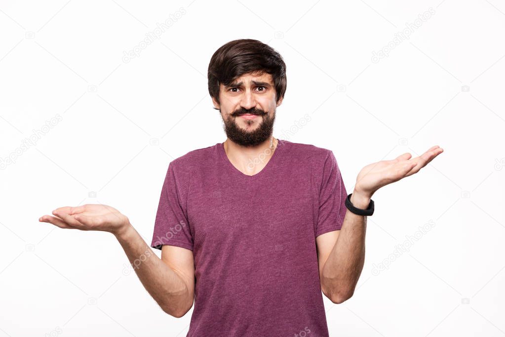 Excited brunet man in a yellow shirt with beard and mostaches shrugging his shoulders being surprised standing isolated over white background. Emotion and gesture of surprise.