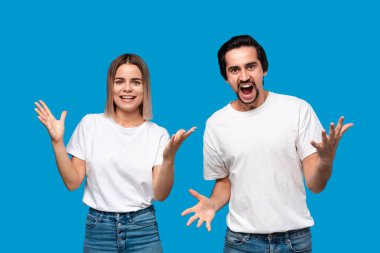 Mutlu çift başarı duygularını ifade ediyor. Genç sarışın kadın ve beyaz tişörtlü bıyıklı ve mavi kot pantolonlu sakallı adam birinci oldu. Mavi arka plan üzerinde izole duran modeller.