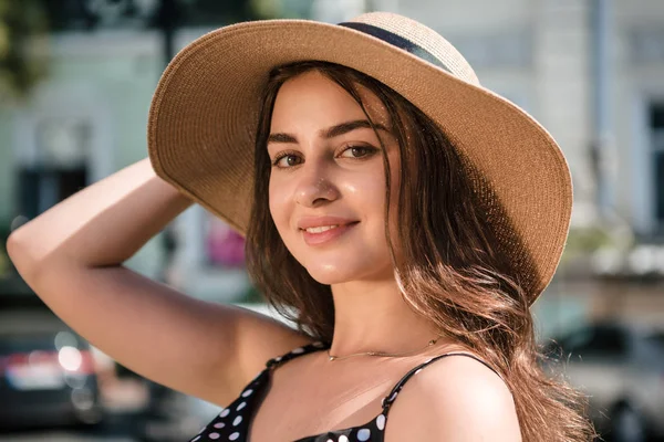 Chica bonita con un vestido negro y un sombrero con amplias aletas sonrisas disfrutando de caminar por la ciudad europea durante el soleado día de verano. Viajar en temporada cálida . — Foto de Stock