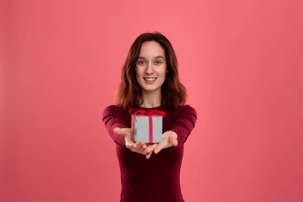 Emocionado chica morena bonita sosteniendo la caja de regalo con una cinta con dos manos de pie aislado sobre un fondo de color rosa oscuro y sonriendo a la cámara. Celebración de un evento especial . —  Fotos de Stock