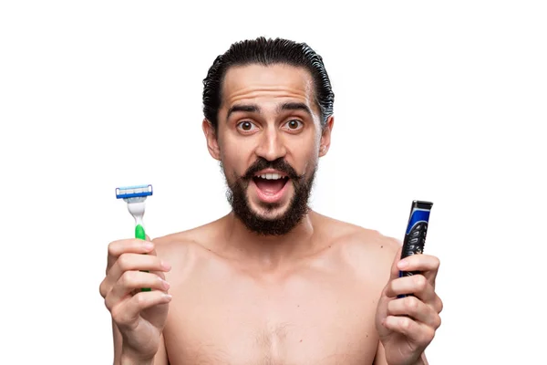Handsome bearded man with mustache holds electric razor and shaving stick standning bare isolated over white background. Concept of morning treatment and shaving. Time to trim your beard.