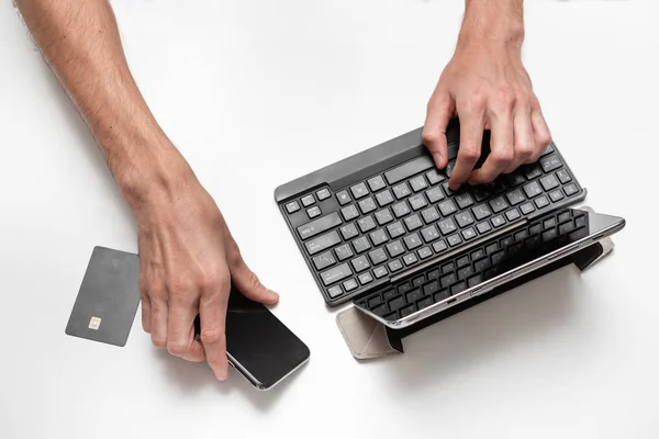 Vista superior cercana de un hombre que trabaja en un proyecto usando una tableta digital con asientos para teclado en una mesa blanca. Smartphone y tarjeta bancaria está cerca de la tableta. Tecnologías modernas en el trabajo . —  Fotos de Stock