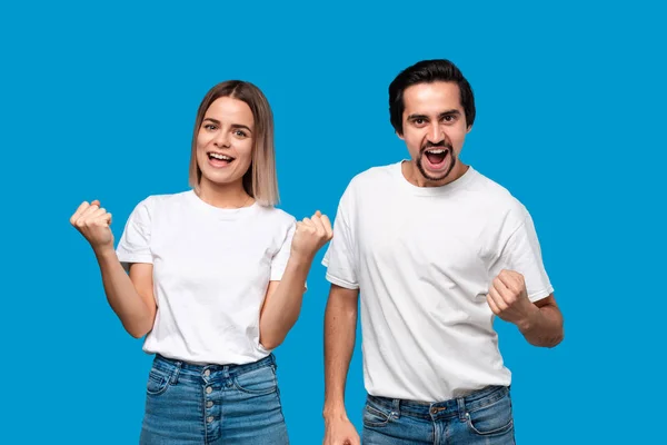 Emotional couple expressing gesture of success. Young blond woman and bearded man with mustaches in white tees and blue jeans are winner.