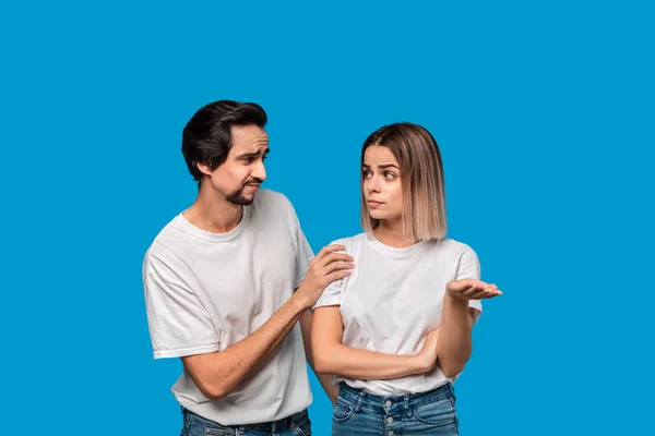 Brunet bearded man with mustaches in white t-shirt and blue jeans trying to cheer up his friend isolated over blue background. Concept of support.