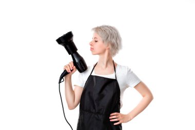 Beyaz tee ve siyah önlük profesyonel siyah saç kurutma makinesi beyaz arka plan izole iş için hazır tutan genç güzel kuaför. Sağlıklı yaşam endüstrisi ve profesyonel kariyer. Profesyonellere güvenin.