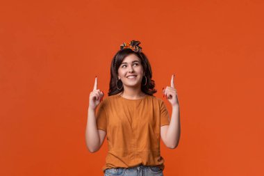 Bir t-shirt ve güzel kafa bandı turuncu arka plan üzerinde izole parmaklarıile işaret Güzel esmer kadın. Reklam yeri.