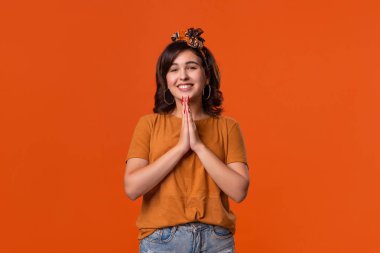 Turuncu bir t-shirt ve güzel bir kafa bandı ile gülümseyen esmer kadın bir rüya gerçek turuncu arka plan üzerinde izole ayakta gerçek olmak isteyen itiraz bir jest el ele tutuşuyor. Rüya kavramı.