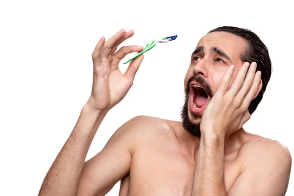 Frightened bearded man with mustache looks at the old shaving stick standning bare isolated over white background. Concept of morning treatment and shaving. Time to trim your beard. Morning routine.