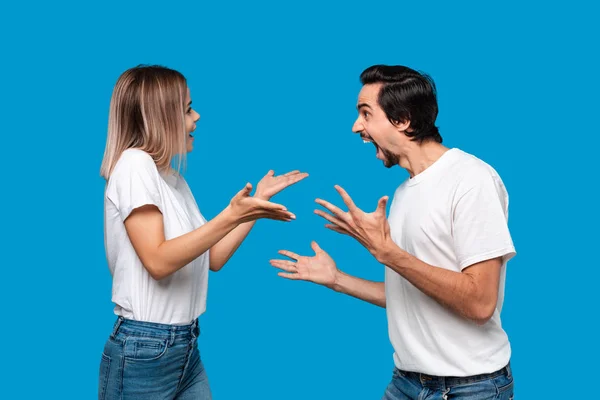 Emotional couple expressing gesture of success. Young blond woman and bearded man with mustaches in white tees and blue jeans are winner. Models standing isolated over blue background. Concept of succ
