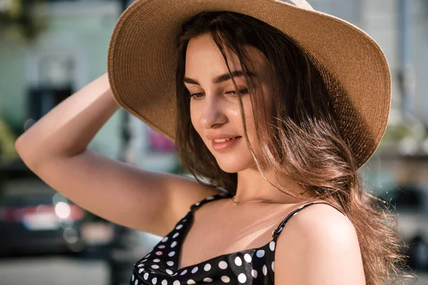 Chica bonita con un vestido negro y un sombrero con amplias aletas sonrisas disfrutando de caminar por la ciudad europea durante el soleado día de verano. Viajar en temporada cálida . — Foto de Stock