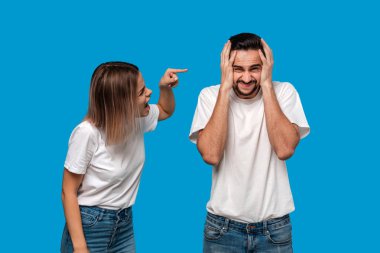 Genç sarışın bir kadın ve beyaz t-shirt ve mavi kot mavi arka plan üzerinde izole ayakta kavga bıyıklı brunet sakallı adam çift. İlişki krizi kavramı. 