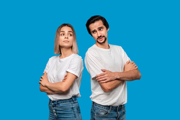 Thoughtful couple of a bearded brunet man with mustache and blond woman in white t-shirts and blue jeands standing isolated over white background.