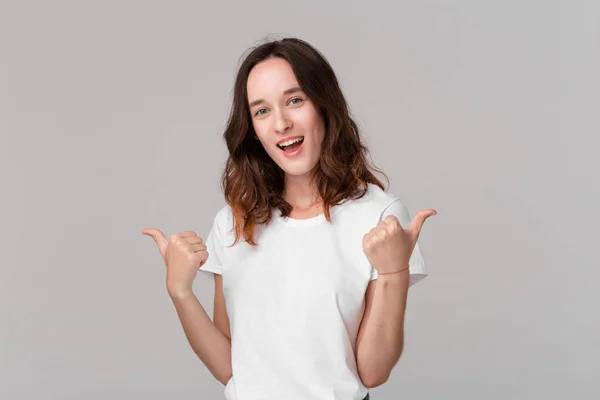 Mooie brunette vrouw in wit t-shirt met duimen omhoog uitdrukken positieve evaluatie permanent geïsoleerd over grijze achtergrond. Ik vind het leuk! — Stockfoto