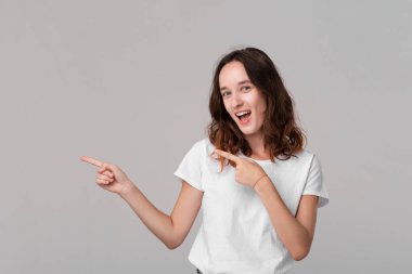 Gri arka plan üzerinde izole duran bir çerçevenin sol tarafında boş alanı işaret beyaz bir tee Pretty esmer kadın. Reklam alanını kopyalama.