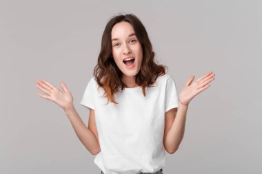 Beyaz bir tee heyecanlı esmer kadın gri arka plan üzerinde izole ayakta sürpriz duygu ifade omuzlarını silkme. Sürpriz duygu.