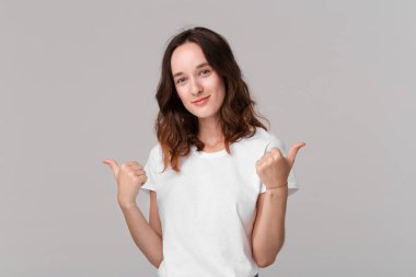Beyaz t-shirt güzel esmer kadın gri arka plan üzerinde izole ayakta olumlu değerlendirme ifade başparmak tutarak. Hoşuma gitti!