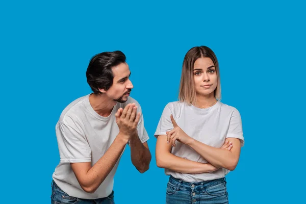 Brunet beyaz t-shirt ve mavi kot bıyıklı adam mavi arka plan üzerinde izole af için kız arkadaşı soran. Suçluluk kavramı.