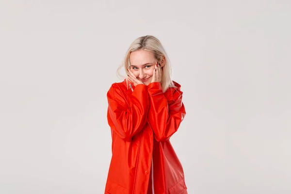 Chica rubia sonriente con un impermeable rojo con capucha aislada sobre fondo blanco. Está empezando a llover. . — Foto de Stock