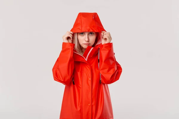 Blond girl gets on hood of a red raincoat isolated over white background. It is starting to rain.