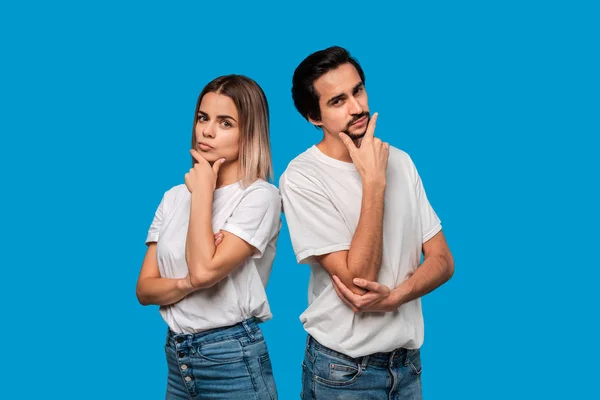 Thoughtful bearded brunet man with mustache and blond woman in white t-shirts and blue jeands standing isolated over white background. Concept of conversation and thinking. — Stock Photo, Image