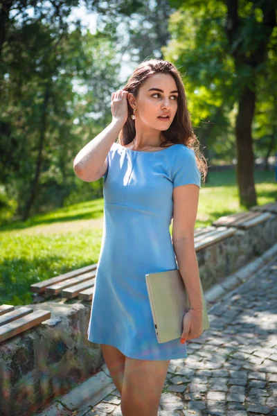 Joven estudiante morena en un vestido azul da un paseo en un parque en un cálido día soleado. La vida en el campus . — Foto de Stock