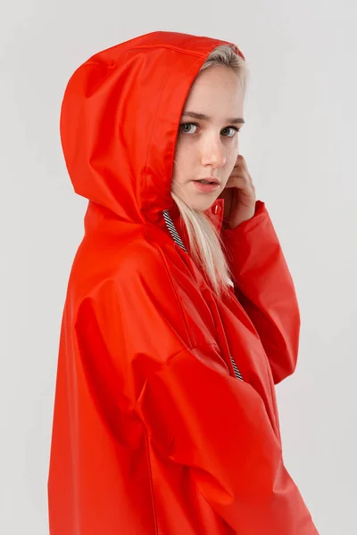 Blond girl gets on hood of a red raincoat isolated over white background. It is starting to rain.