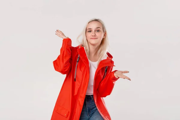 Linda chica rubia con un impermeable rojo y una camiseta blanca de pie aislada sobre fondo blanco. Prepárate para el mal tiempo . —  Fotos de Stock