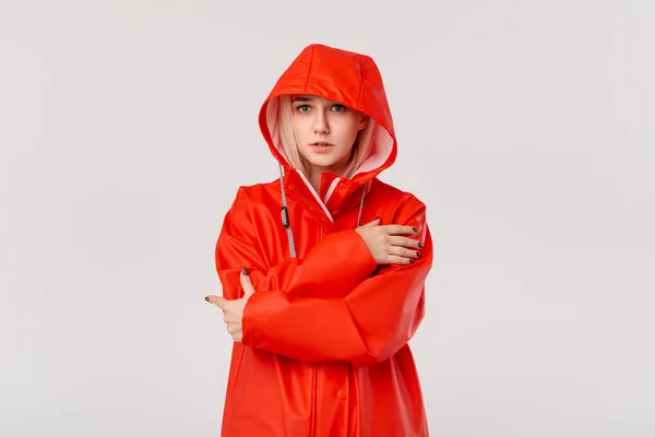 Blond girl in a red raincoat with a hood standing isolated over white background. Are you ready for cold bad weather?
