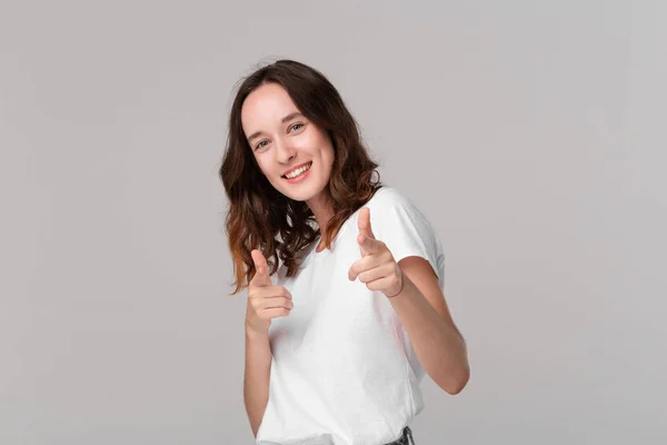 Glimlachend brunette vrouw in het wit een t-shirt wijzend met haar vingers op de camera geïsoleerd over oranje achtergrond. Plaats voor advertentie. — Stockfoto