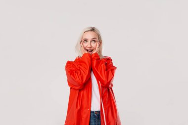 Beyaz arka plan üzerinde izole mutluluk duygularını ifade yüzünün yanında el ele tutuşan kırmızı yağmurluk heyecanlı sarışın kız. Yağmurlu havaiçin hazır olun. Reklam için boş alan