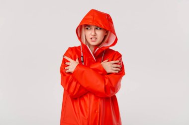 Kapüşonlu kırmızı yağmurluklu sarışın kız beyaz arka plan üzerinde izole ayakta donuyor. Soğuk kötü hava için hazır mısınız?